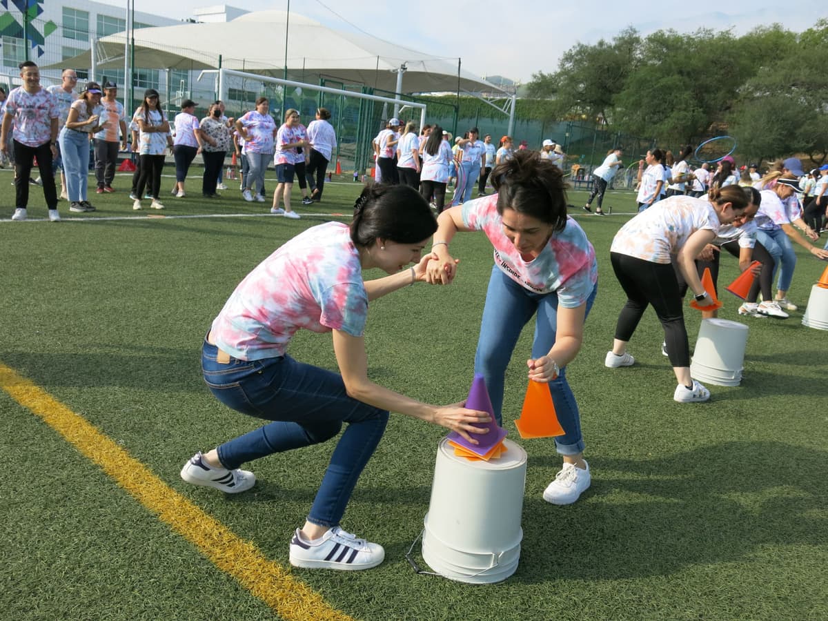 Maestros riendo mientras compiten amistosamente durante una dinámica al aire libre, reforzando la conexión entre colegas