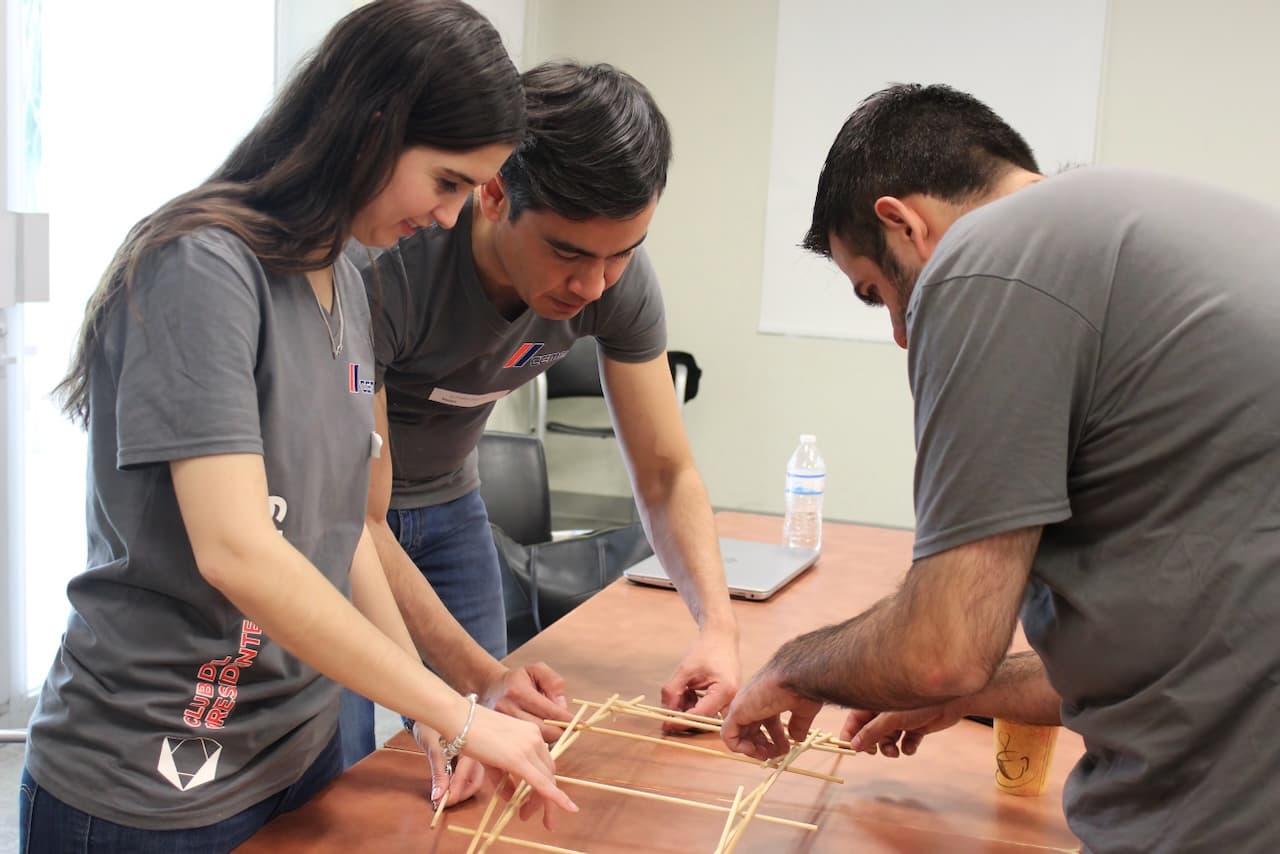 Equipo de ALYAX trabajando juntos en una dinámica en interiores, ensamblando objetos con precisión y colaboración